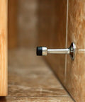 Wall-mounted metal door stopper with black rubber tip on tile floor