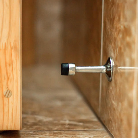 Wall-mounted metal door stopper with black rubber tip on tile floor