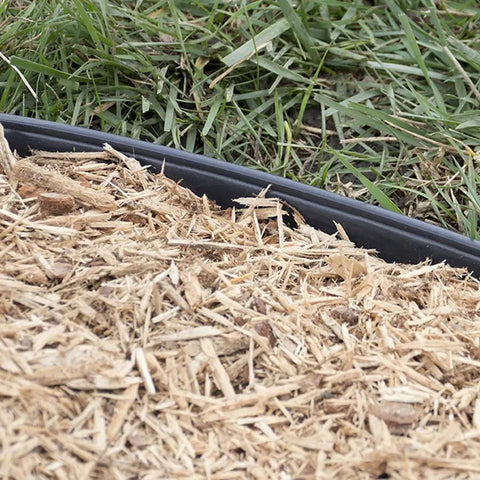 Close-up of Heavy Duty No Dig Edging Kit For Garden Borders with mulch and grass, showing black plastic edge in use.