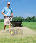 Man using Spyker All Season Spreader Kit Ergo Pro 50 Pound Broadcast Spreader With 25 Pound Bag Spreader on lawn