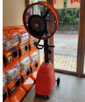 No Sweat Commercial Misting Fan Delivers Beast Mode High Velocity Airflow For Restaurants And Warehouses Featuring Rock Solid Metal Housing And Quick Adjustable Tilt Swivel In Blue, standing near a large window.