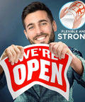 Man holding a red 'We're Open' sign showcasing its flexibility and strength, indicating the material's durability.