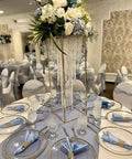 Elegant wedding table setting with floral centerpiece and beaded glass stands on a decorated round table with blue accents.