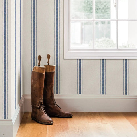 Interior with Blue Linette Fabric Stripe Wallpaper With Canvas Look, Textured Stripes, near window with boots on wooden floor.
