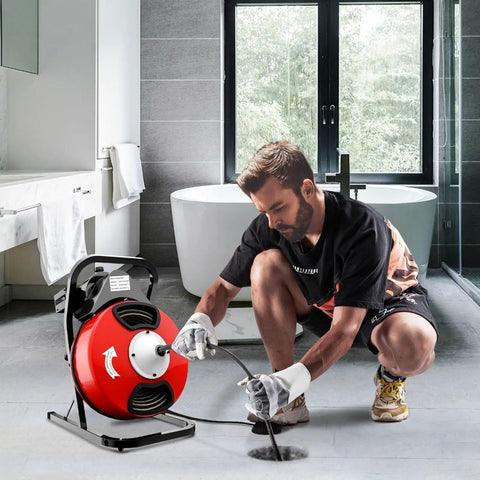 Man using Heavy Duty Electric Drain Auger With Sharp Rotary Blades And Foot Switch For Smashing Backed Up Lines In One To Four Inch Pipes Using Tangle Free Steel Core Snake in a bathroom setting.