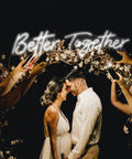 Couple under Better Together Neon Sign With Remote, Large Two Part Wedding Decor Kit, surrounded by guests taking photos