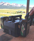 Hand holding 4-Port Battery Charger For 18V And 36V Slide-Style Batteries With Rapid Charging, USB, and AC outlets on worksite desk.