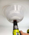 Front view of a clear plastic dust bowl attachment mounted on a yellow cordless drill for hole saws (recessed lighting).