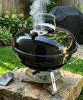 Black kettle grill with Cool Touch Damper Handle for Smokey Mountain WSM Kettle Grill, steam visible in a garden setting
