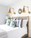 Gold Brass Industrial Swing Arm LED Wall Sconce with Adjustable Metal Shade over a bedroom bed in farmhouse style setting.