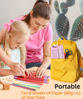 Child using Pink A5 Paper Cutter Guillotine with Side Ruler for scrapbooking, supervised by adult, bright yellow backpack nearby.