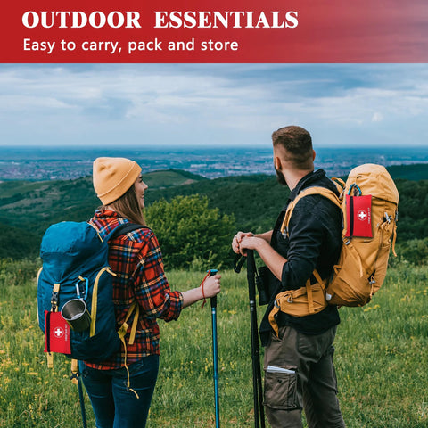 Two red mini first aid kits attached to blue and tan hiking backpacks in an outdoor meadow.