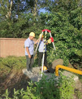 Two workers using Rugged Confined Space Tripod Rescue Rig Featuring Heavy Duty Winch Choices next to a manhole outdoors.