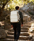 Person hiking with Go-To Travel Backpack for Women and Men Carry On Luggage Flight Ready Personal Item Essentials Waterproof Laptop Backpack Large Capacity Daypack Brown Beige.
