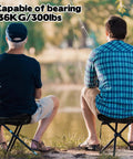 Two people fishing while sitting on Portable Tripod Folding Camping Stools, 14.6 inch seat, black, supports up to 210 lbs