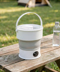 Compact Folding Mini Washing Machine Portable Laundry Basin on wooden table outdoors, ideal for road trips and dorms.