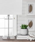 Toledo 25 Inch Crystal Table Lamp With Cotton Shade on side table next to potted plant and decorative objects in living room.