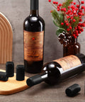 Top Shelf Black PVC Heat Shrink Bottle Caps With Ridiculously Slick Finish For Wine And Hot Sauce Packaging 200 Piece Box Fits 5 Ounce Wide Woozy Bottles on wine bottles with wooden cutting board backdrop.