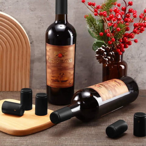 Top Shelf Black PVC Heat Shrink Bottle Caps With Ridiculously Slick Finish For Wine And Hot Sauce Packaging 200 Piece Box Fits 5 Ounce Wide Woozy Bottles on wine bottles with wooden cutting board backdrop.