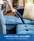 Quiet Bagless Canister Vacuum With Kickass Suction For Whole Home Cleaning Slick Tile Floors and Low Pile Carpets Plus Retractable Cord and Fast Dump Dust Cup For Smooth Daily Sweepups using crevice tool on a blue couch.