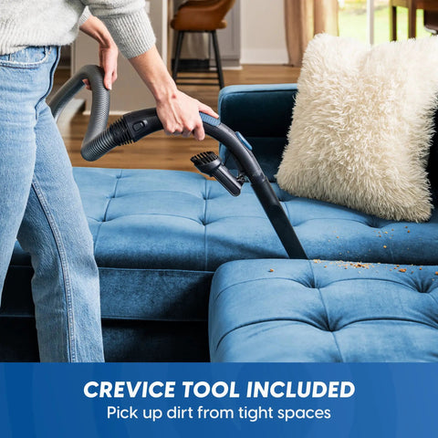 Quiet Bagless Canister Vacuum With Kickass Suction For Whole Home Cleaning Slick Tile Floors and Low Pile Carpets Plus Retractable Cord and Fast Dump Dust Cup For Smooth Daily Sweepups using crevice tool on a blue couch.