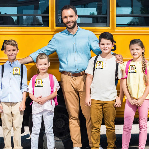 Bus Themed 24 Pack Kid Friendly School Name Plates worn by children with a teacher in front of a school bus