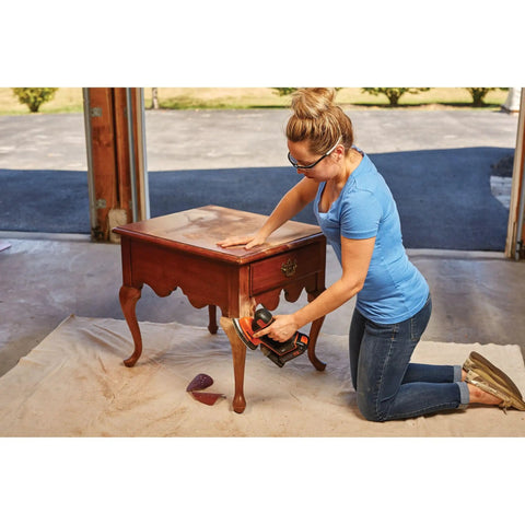 Person using 20V Max Sheet Sander with 12,000 OPM on wooden table, showcasing detail finger attachment for tight surfaces