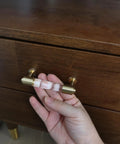 Hand holding brass and clear acrylic kitchen cabinet pull on dresser drawer.