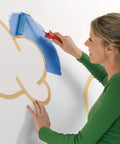 Woman painting with blue paint using Masking Tape For Curves Ultra Flexible 19mm By 25m Pro Grade Tape on a wall.