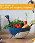 Pastail Medium Whale Shaped Pasta Colander for draining pasta, vegetables, and fruit on countertop with produce inside