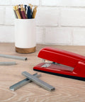 Premium One Quarter Inch Staples, 210 Per Strip, Five Pack, scattered on desk with stapler and pen holder