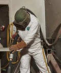 Worker in MicroMax Protective Disposable Coveralls For Paint Job And Cleanup With Respirator Fit Hood using equipment on job site