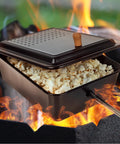 Campfire Popcorn Popper for Open Flame Cooking with Nonstick Finish and Extended Handle, filled with popcorn over a fire.