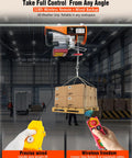 Orange electric hoist lifts a pallet of boxes in a warehouse; yellow wired remote and red wireless remote in foreground.