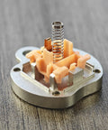 Cherry MX-style switch with peach-colored housing and stainless steel coil spring, close-up view.