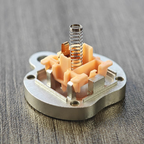 Cherry MX-style switch with peach-colored housing and stainless steel coil spring, close-up view.
