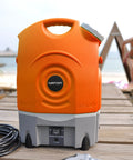 On The Go Portable Spray Washer With Built In Water Tank, showing orange tank, black hose, on wooden deck by beach