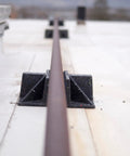 Saddle rooftop pipe stand with brown pipe in a black plastic cradle on a flat roof.
