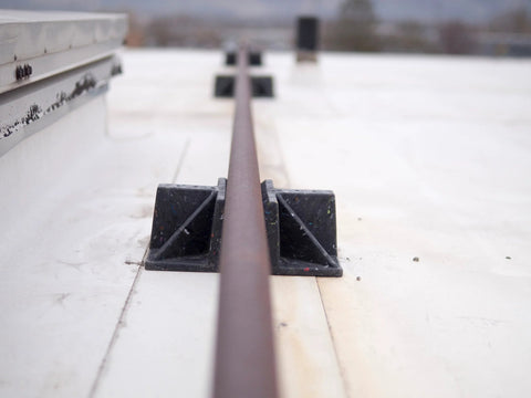 Saddle rooftop pipe stand with brown pipe in a black plastic cradle on a flat roof.