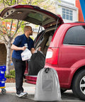 Man loading car with 2 Pack Travel Laundry Bags With Handles And Aluminum Carabiner Dirty Clothes Organizer in red vehicle trunk.