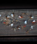 Rustic wood surface with hand-tied flies from 30 Piece Fly Fishing Lure Kit Hand Tied Dry Wet Streamers And Nymph Flies For Trout Bass Salmon Assortment Premium Angler Set Realistic Flies For Freshwater Adventures displayed.