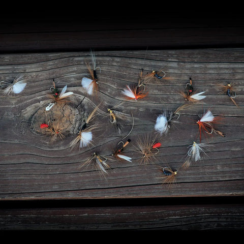 Rustic wood surface with hand-tied flies from 30 Piece Fly Fishing Lure Kit Hand Tied Dry Wet Streamers And Nymph Flies For Trout Bass Salmon Assortment Premium Angler Set Realistic Flies For Freshwater Adventures displayed.