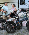 Two people standing beside Beast 1400W Peak Electric Bike for Adults with Full Suspension and Fat Tires near an RV.