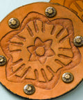 Round orange leather coaster with a debossed floral design and metal studs
