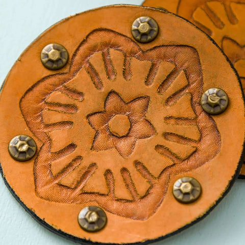 Round orange leather coaster with a debossed floral design and metal studs