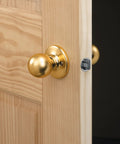 Close-up of a golden door knob on a wooden door, showing installation using Door Lock Installation Kit With C Clamp Design Hole Saw For Metal Or Wood Doors 2 Adjustable Bushings Tool Free Clamping Easy Height Alignment Accurate Drilling Pro Grade And User Friendly.