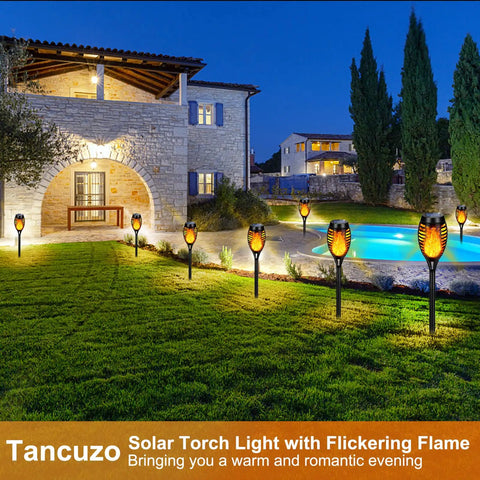Outdoor Solar Torch Lights 6 Pack With Flickering Flame illuminating garden near stone house at night