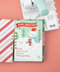 Mini Cinch Binding Tool For DIY Books And Notebooks With Wire Or Spiral Coils Pro Grade Mini Binding Machine next to a Christmas-themed notebook