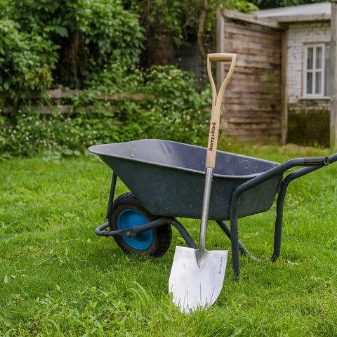 Round Point Gardening Shovel With Wood D Handle 41 Inch Steel Digging Spade for Lawn Yard next to wheelbarrow in garden
