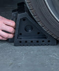 Solid Rubber Wheel Chocks With Traction Ribs For That Tire Grip And A Handy Handle For Quick Positioning Built Tough To Keep Your Ride Secured On Slopes placed behind a vehicle tire on concrete surface